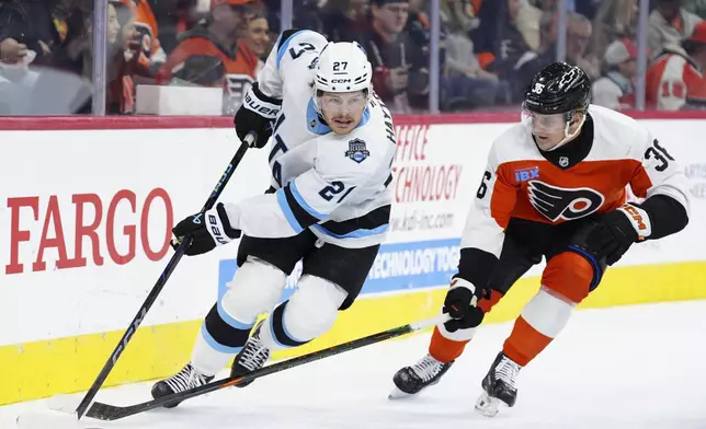 Utah Hockey Club's Barrett Hayton, left, skates with the puck past the defense of Philadelphia Flyers' Emil Andrae during the first period of an NHL hockey game, Sunday, Dec. 8, 2024, in Philadelphia. (AP Photo/Derik Hamilton)