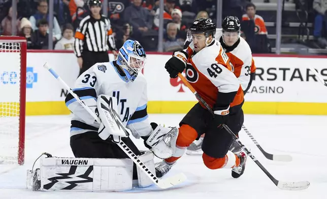 Utah Hockey Club goaltender Jaxson Stauber, left, looks to block a shot past the screen of Philadelphia Flyers' Morgan Frost (48) during the second period of an NHL hockey game, Sunday, Dec. 8, 2024, in Philadelphia. (AP Photo/Derik Hamilton)