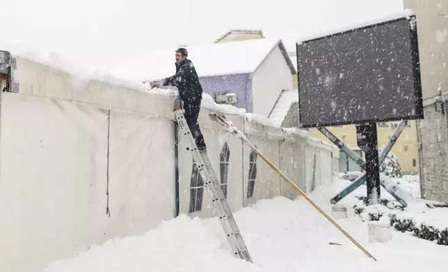 A man clears snow from a tent during heavy snowfall in Bihac, Bosnia, Monday, Dec. 23, 2024. (AP Photo/Edvin Zulic)