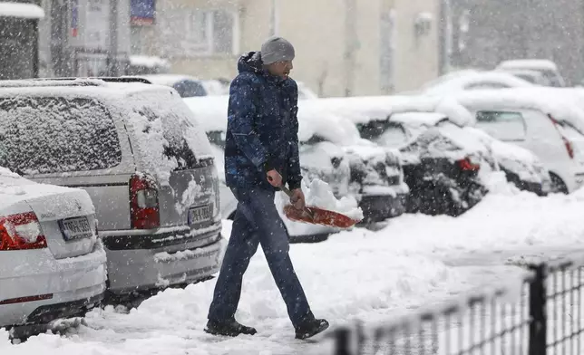 A man shovels snow from the street during heavy snowfall in Bihac, Bosnia, Monday, Dec. 23, 2024. (AP Photo/Edvin Zulic)