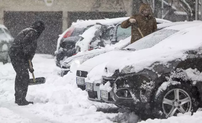 A man shovels snow from the street during heavy snowfall in Bihac, Bosnia, Monday, Dec. 23, 2024. (AP Photo/Edvin Zulic)