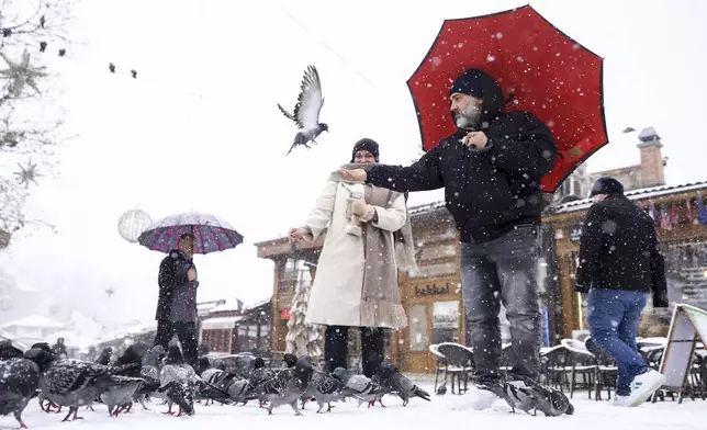 Tourists feed pigeons during heavy snowfall in downtown Sarajevo, Bosnia, Monday, Dec. 23, 2024. (AP Photo/Armin Durgut)