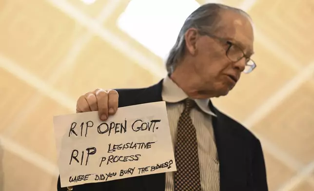 A protestor holds a sign as the Republican-dominated North Carolina House convened to complete the override of Gov. Cooper's veto, Wednesday, Dec. 11, 2024, in Raleigh, N.C. (AP Photo/Matt Kelley)