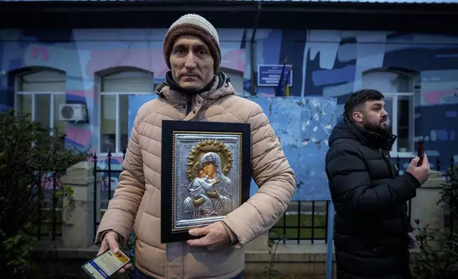 A man holds a religious icon outside the closed voting station where Calin Georgescu, an independent candidate for president who won the first round of presidential elections, was supposed to vote, after Romania's Constitutional Court annulled the first round of presidential elections, in Mogosoaia, Romania, Sunday, Dec. 8, 2024. (AP Photo/Andreea Alexandru)