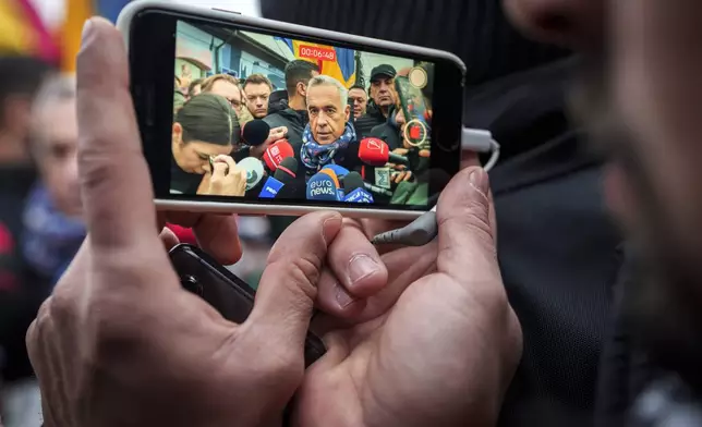 A man records video of Calin Georgescu, an independent candidate for president who won the first round of presidential elections, speaking to media outside a closed voting station after Romania's Constitutional Court annulled the first round of presidential elections, in Mogosoaia, Romania, Sunday, Dec. 8, 2024. (AP Photo/Vadim Ghirda)