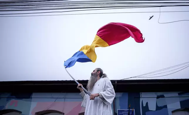 A man waves the Romanian flag outside the closed voting station where Calin Georgescu, an independent candidate for president who won the first round of presidential elections, was supposed to vote, after Romania's Constitutional Court annulled the first round of presidential elections, in Mogosoaia, Romania, Sunday, Dec. 8, 2024. (AP Photo/Andreea Alexandru)