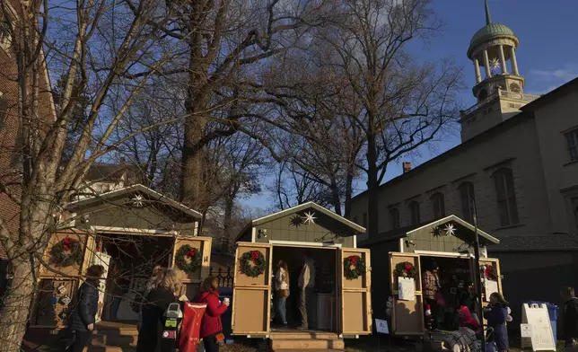 People shop at Christmas-themed wooden huts located next to the Central Moravian Church in Bethlehem, Pa., on Sunday, Dec. 1, 2024. (AP Photo/Luis Andres Henao)