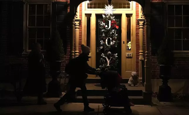 A woman pushes a stroller in front of a house decorated with a Moravian star and Christmas wreaths in Bethlehem, Pa., on Sunday, Dec. 1, 2024. (AP Photo/Luis Andres Henao)