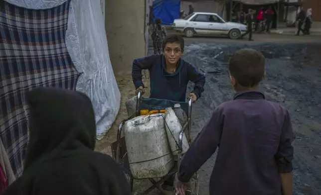 A Palestinian boy pushes a wheelchair carrying jerrycans and plastic bottles with water at a camp for displaced people in Deir al-Balah, Gaza Strip, Thursday, Dec. 12, 2024. (AP Photo/Abdel Kareem Hana)