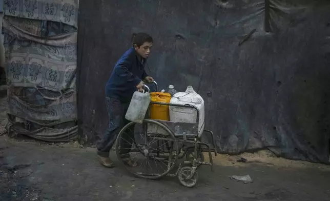 A Palestinian boy pushes a wheelchair carrying jerrycans and plastic bottles with water at a camp for displaced people in Deir al-Balah, Gaza Strip, Thursday, Dec. 12, 2024. (AP Photo/Abdel Kareem Hana)