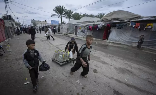 Palestinian children push a cart carrying jerrycans and plastic bottles of water at a camp for displaced people in Deir al-Balah, Gaza Strip, on Thursday, Dec. 12, 2024. (AP Photo/Abdel Kareem Hana)