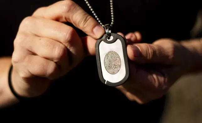 Jen Dold, whose brother, Alex Dold, lived with schizophrenia and died after a 2017 encounter with sheriff's deputies and police officers, holds a dog tag with her brother's fingerprint she wears around her neck Wednesday, Sept. 18, 2024, at a favorite beach of his in Edmonds, Wash. (AP Photo/Lindsey Wasson)