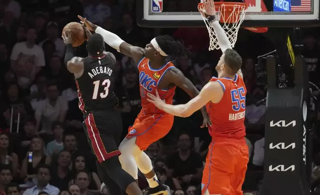 Oklahoma City Thunder guard Luguentz Dort (5) blocks a drive to the basket by Miami Heat center Bam Adebayo (13) during the first half of an NBA basketball game, Friday, Dec. 20, 2024, in Miami. (AP Photo/Marta Lavandier)