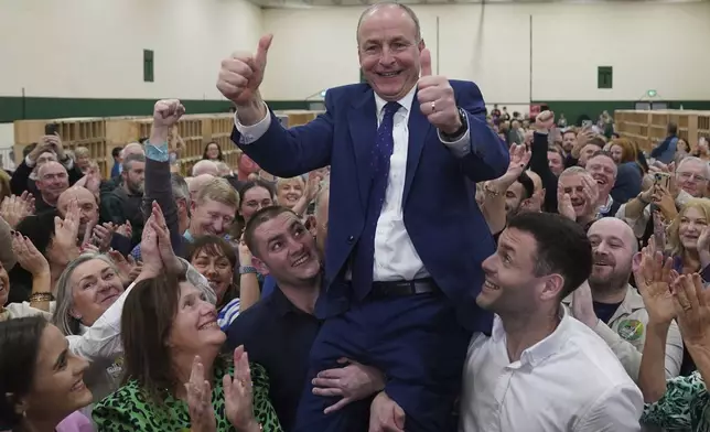 Fianna Fail leader Micheal Martin is hoisted up by his sons Cillian and Micheal Aodh, after he was deemed elected in the Cork South Central constituency at the election count centre at Nemo Rangers GAA Club in Cork, after the General Election, Saturday, Nov. 30, 2024. (Jacob King/PA via AP)