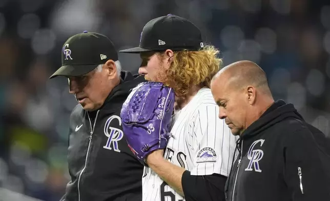 FILE - Colorado Rockies relif pitcher Noah Davis, center, is escorted from the mound by manager Bud Black, back, and assistant trainer Heath Townsend after suffering an injury in the seventh inning in the second baseball game of a doubleheader against the Seattle Mariners, Sunday, April 21, 2024, in Denver. (AP Photo/David Zalubowski, File)