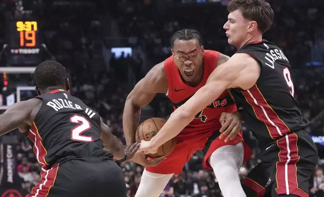 Toronto Raptors' Scottie Barnes (4) drives against Miami Heat's Pelle Larsson (9) and Terry Rozier (2) during first-half NBA basketball game action in Toronto, Sunday, Dec. 1, 2024. (Chris Young/The Canadian Press via AP)