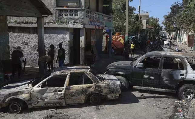 Residents walk past cars set on fire by armed gangs in the Poste Marchand neighborhood of Port-au-Prince, Haiti, Tuesday, Dec. 10, 2024. (AP Photo/Odelyn Joseph)