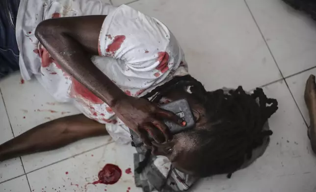 A wounded journalist talks on the phone after being shot by armed gangs at the General Hospital in Port-au-Prince, Haiti, Tuesday, Dec. 24, 2024. (AP Photo/Jean Feguens Regala)