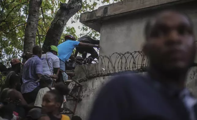 Journalists climb up a wall to take cover from gunfire, after being shot at by armed gangs at the General Hospital in Port-au-Prince, Haiti, Tuesday, Dec. 24, 2024. (AP Photo/Jean Feguens Regala)