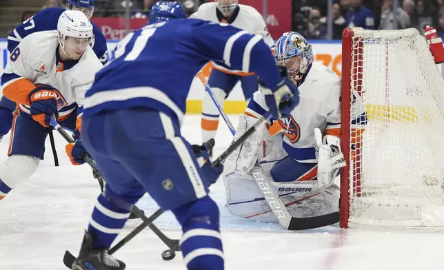 Toronto Maple Leafs center John Tavares (91), New York Islanders defenseman Alexander Romanov (28) and Islanders goaltender Ilya Sorokin (30) battle for the loose puck during the second period of an NHL hockey game in Toronto, Saturday, Dec. 21, 2024. (Frank Gunn/The Canadian Press via AP)