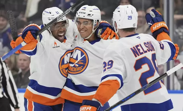 New York Islanders defenseman Isaiah George, center, celebrates after his first NHL goal with teammates Anthony Duclair (11) and Brock Nelson (29) during third-period hockey game action against the Toronto Maple Leafs in Toronto, Saturday, Dec. 21, 2024. (Frank Gunn/The Canadian Press via AP)