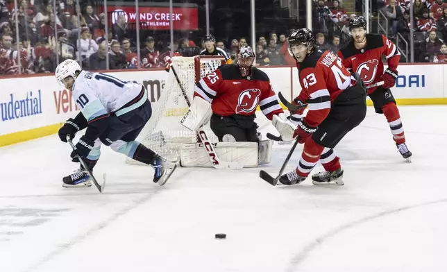 New Jersey Devils goaltender Jacob Markstrom (25), watches as defenseman Luke Hughes (43) and Seattle Kraken center Matty Beniers (10) turn to chase the puck during the third period of an NHL hockey game against the Seattle Kraken, Friday, Dec. 6, 2024, in Newark, N.J. Devils won 3-2. (AP Photo/Stefan Jeremiah)