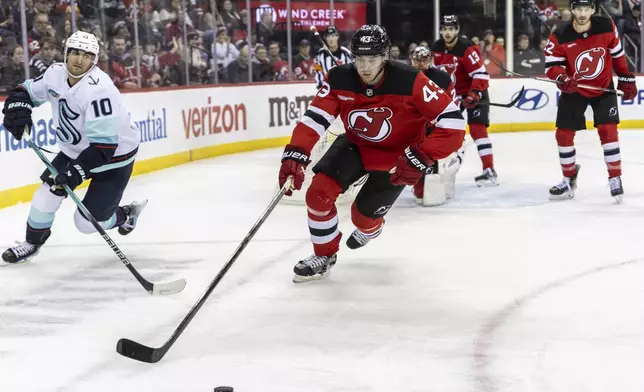 New Jersey Devils defenseman Luke Hughes (43) and Seattle Kraken center Matty Beniers (10) chase the puck during the third period of an NHL hockey game against the Seattle Kraken, Friday, Dec. 6, 2024, in Newark, N.J. Devils won 3-2. (AP Photo/Stefan Jeremiah)