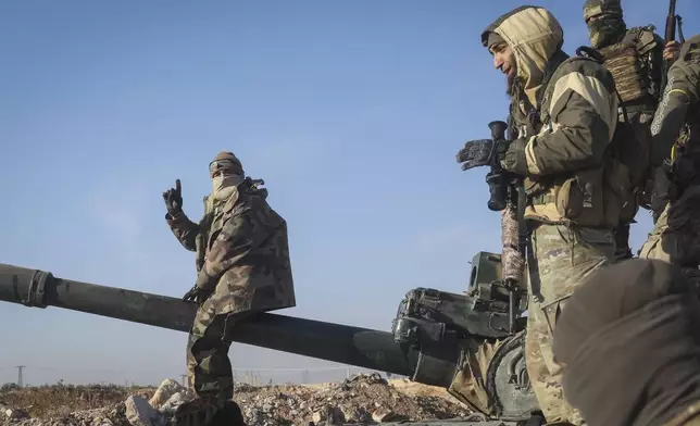 Syrian opposition fighters stand atop a seized military armored vehicle on the outskirts of Hama, Syria, Tuesday, Dec. 3, 2024. (AP Photo/Ghaith Alsayed)