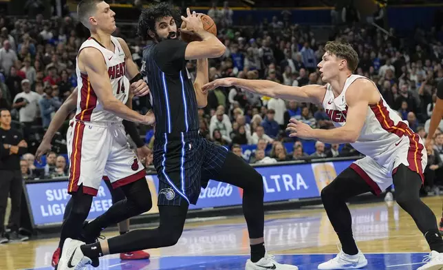 Orlando Magic center Goga Bitadze, center, makes a move to the basket against Miami Heat guard Tyler Herro, left, and guard Pelle Larsson during the second half of an NBA basketball game, Saturday, Dec. 21, 2024, in Orlando, Fla. (AP Photo/John Raoux)