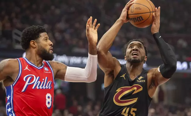 Cleveland Cavaliers' Donovan Mitchell (45) shoots as Philadelphia 76ers' Paul George (8) defends during the first half of an NBA basketball game in Cleveland, Saturday, Dec. 21, 2024. (AP Photo/Phil Long)