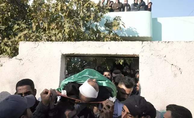 Mourners carry the body of Akram Abu Arrah, wrapped with a Hamas flag, out of the family house during his funeral with Mohammad Ghannam, both killed in an airstrike Israel said targeted a militant cell, in the West Bank village of Al-Aqaba, Tuesday Dec. 3, 2024. (AP Photo/Majdi Muhammad)