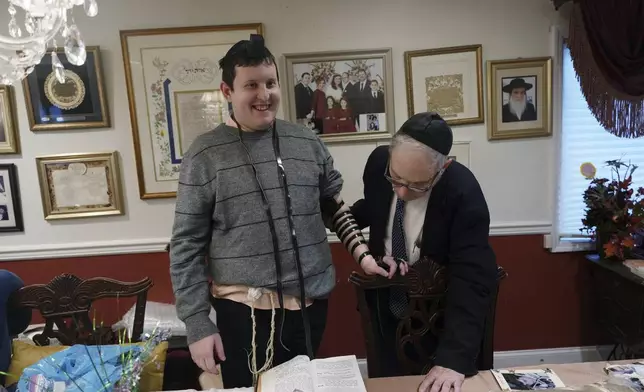 Dov Marcus smiles after wrapping the leather straps of tefillin to pray with his uncle, Chaim Orlan, in Teaneck, N.J., on Friday, Dec. 20, 2024. (AP Photo/Luis Andres Henao)