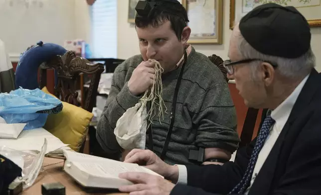 Dov Marcus, left, kisses the knotted fringes -- known as tzitzit – of his prayer shawl after wrapping the leather straps of tefillin and praying with his uncle, Chaim Orlan, in Teaneck, N.J., on Friday, Dec. 20, 2024. (AP Photo/Luis Andres Henao)