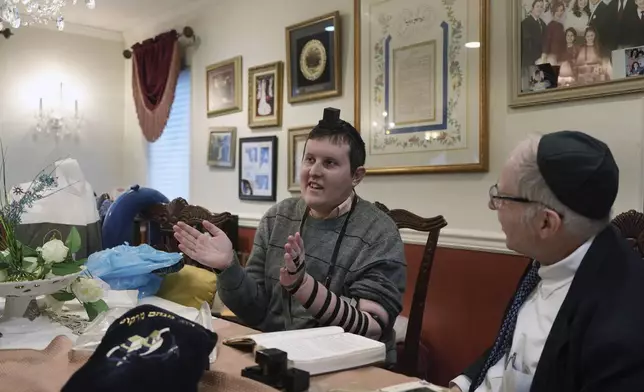 Dov Marcus, left, sings with his mother, Debbie Marcus, after wrapping the leather straps of tefillin and praying with his uncle, Chaim Orlan, right, in Teaneck, N.J., on Friday, Dec. 20, 2024. (AP Photo/Luis Andres Henao)