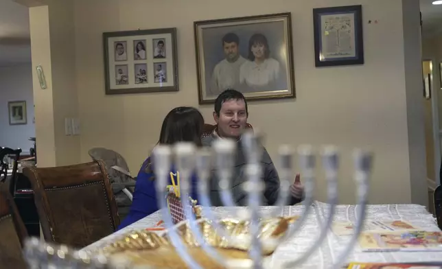 Dov Marcus talks to his mother, Debbie Marcus, at their dining table near the branched candelabra called a menorah, in Teaneck, N.J., on Friday, Dec. 20, 2024. (AP Photo/Luis Andres Henao)