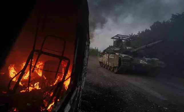 A Ukrainian tank passes by a burning car near the Russian-Ukrainian border, Sumy region, Ukraine, Wednesday, Aug. 14, 2024. (AP Photo/Evgeniy Maloletka)