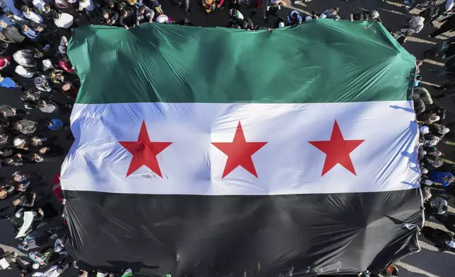 Syrians display a giant Syrian "revolutionary" flag during a celebratory demonstration following the first Friday prayers since Bashar Assad's ouster, in Damascus' central square, Syria, Friday, Dec. 13, 2024. (AP Photo/Ghaith Alsayed)