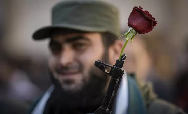 A Syrian fighter holds a gun with a flower placed in the barrel, as people gather for Friday prayers at the Umayyad mosque in Damascus, Syria, Friday, Dec. 13, 2024. (AP Photo/Leo Correa)