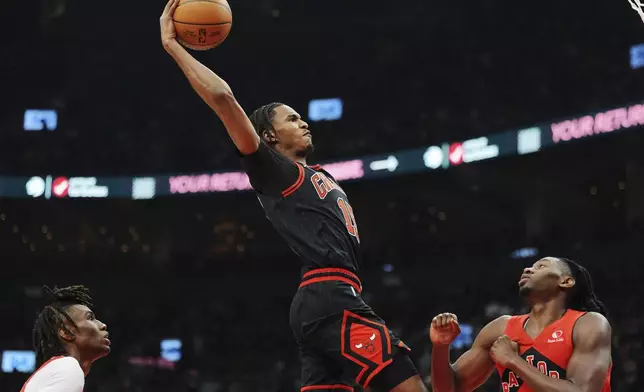 Chicago Bulls' Julian Phillips, center, goes up to dunk between Toronto Raptors' Ja'Kobe Walter, left, and Jonathan Mogbo, right, during first-half NBA basketball game action in Toronto, Monday, Dec. 16, 2024. (Frank Gunn/The Canadian Press via AP)