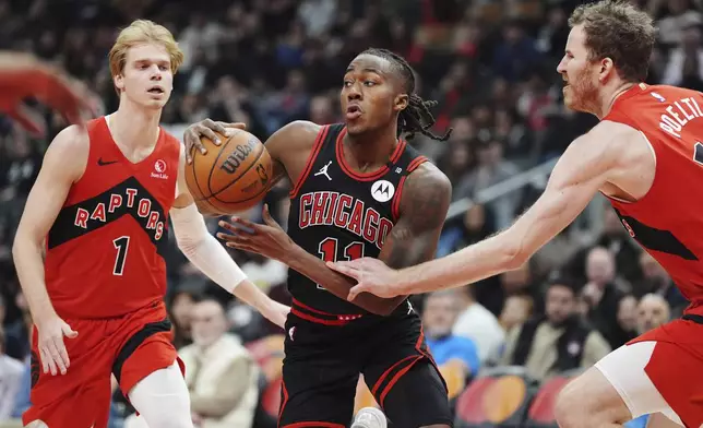 Chicago Bulls' Ayo Dosunmu (11) drives between Toronto Raptors' Gradey Dick (1) and Jakob Poeltl, right, during first-half NBA basketball game action in Toronto, Monday, Dec. 16, 2024. (Frank Gunn/The Canadian Press via AP)