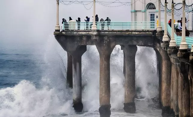 People stand at the end of the Manhattan Beach Pier and watch high surf pound the pylons on Tuesday, Dec. 24, 2024 in Manhattan Beach, Calif. (AP Photo/Richard Vogel)