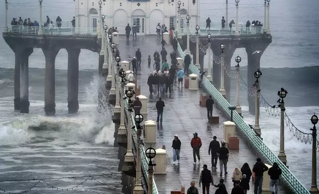 People brave the rain and walk along the Manhattan Beach Pier to watch high surf on Tuesday, Dec. 24, 2024 in Manhattan Beach, Calif. (AP Photo/Richard Vogel)