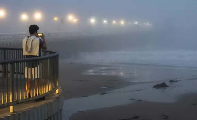 A person takes a photo of high surf near the Santa Cruz Wharf in Santa Cruz, Calif., Monday, Dec. 23, 2024. (AP Photo/Nic Coury)