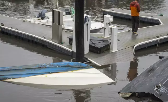 A man walks by overturned boats in Santa Cruz Harbor in Santa Cruz, Calif., Tuesday, Dec. 24, 2024. (AP Photo/Nic Coury)