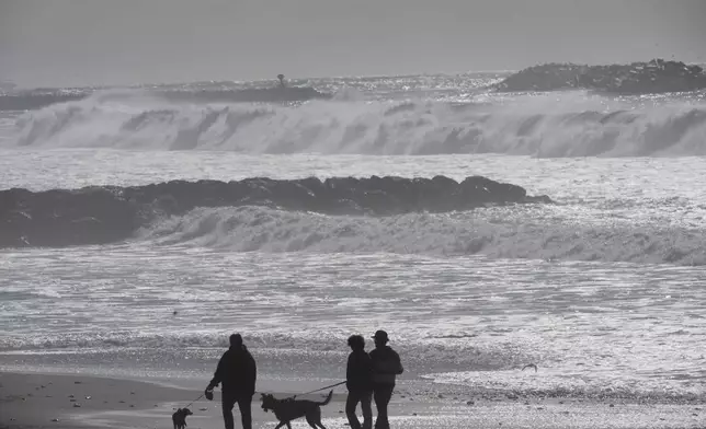 Visitors walk along the beach as high surf comes in Ventura, Calif., Tuesday, Dec. 24, 2024. (AP Photo/Damian Dovarganes)