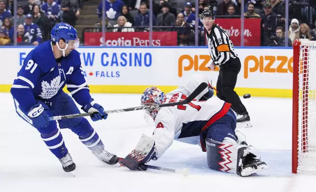 Toronto Maple Leafs center John Tavares (91) scores against Washington Capitals goaltender Charlie Lindgren, front right, during second-period NHL hockey game action in Toronto, Friday, Dec. 6, 2024. (Cole Burston/The Canadian Press via AP)dian Press via AP)