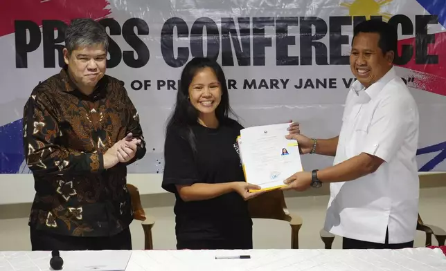 Mary Jane Veloso, center, a Filipina who was on death row in Indonesia and was nearly executed by firing squad in 2015, receives her transfer document from acting Deputy Coordinating Minister for Immigration and Correctional Affairs I Nyoman Gede Surya Mataram as Philippine's Undersecretary for Migration Affairs at the Department of Foreign Affairs Eduardo Jose de Vega, left, applauds during a handover ceremony prior to her repatriation to the Philippines, at Soekarno-Hatta International Airport in Tangerang, Indonesia, Tuesday, Dec. 17, 2024. (AP Photo/Tatan Syuflana)