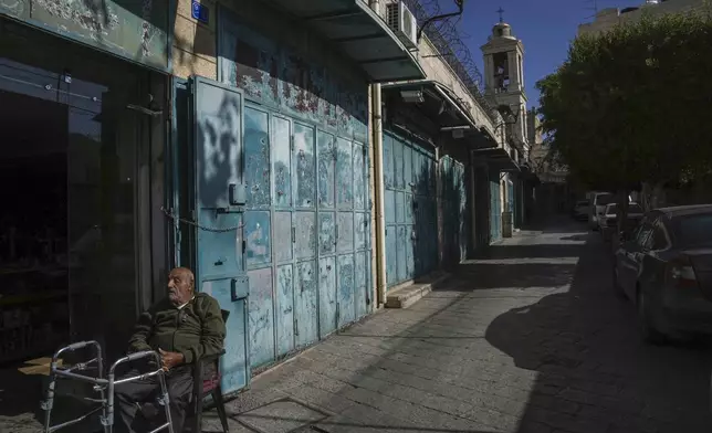 A man rests by a row of empty shops near the Church of the Nativity, where Christians believe Jesus Christ was born, ahead of Christmas in the West Bank city of Bethlehem, Tuesday, Dec. 17, 2024. (AP Photo/Mahmoud Illean)