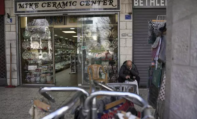 A man waits outside a souvenir shop near the Church of the Nativity, where Christians believe Jesus Christ was born, ahead of Christmas in the West Bank city of Bethlehem, Saturday Dec. 21, 2024. (AP Photo/Mahmoud Illean)