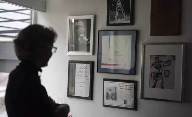 Two-time Olympian Joan Wilder looks at memorabilia at her home on Nov. 22, 2024, in Bend, Ore., including an image of her competing at bottom right. (AP Photo/Jenny Kane)